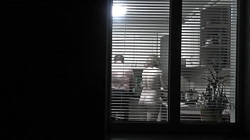 Peeping. Voyeur. Neighbor perv Hidden cam in evening on street looks out window as bare sumptuous neighbor in kitchen preps dinner for her husband. bare in public. bare at home. Family.  Outdoor